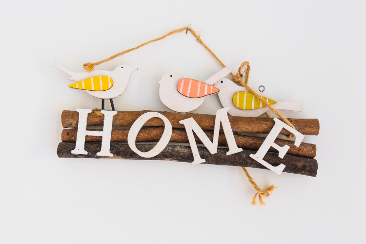 A dark wooden sign against a blank wall with the word home on it. Wooden birds sit on top.